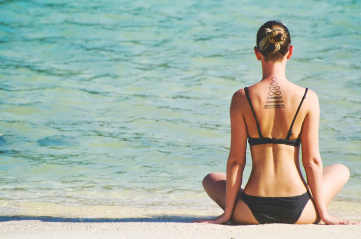 woman meditation on beach with spiral tattoos