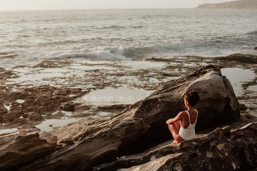 woman sitting on rocky beach saying morning affirmations