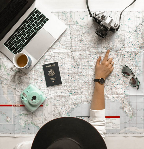 planning travel tips - woman pointing finger at map with computer, passport, and camera